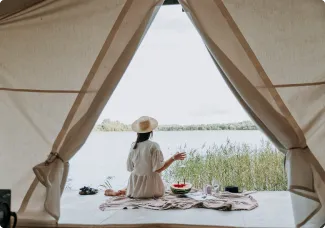 米色的大帳篷底下有一個帶著草帽的女人坐著看像湖面